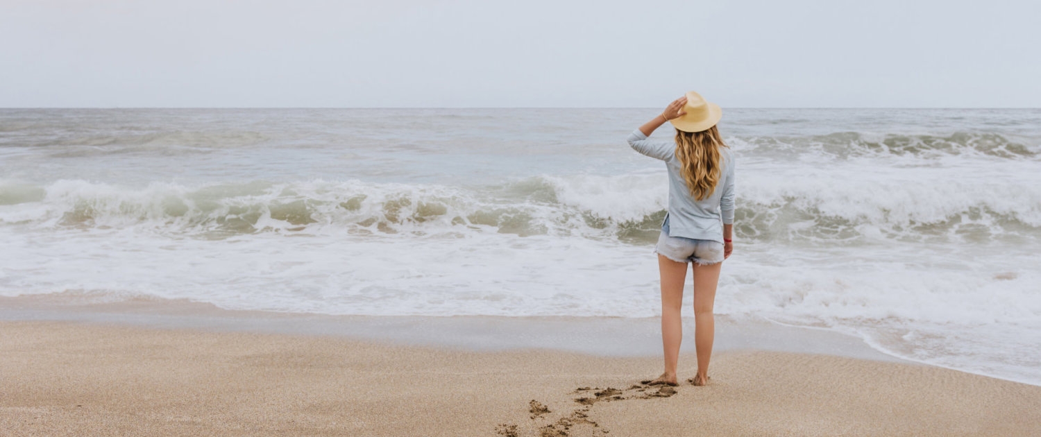 the girl in the hat on the beach looking at the sea