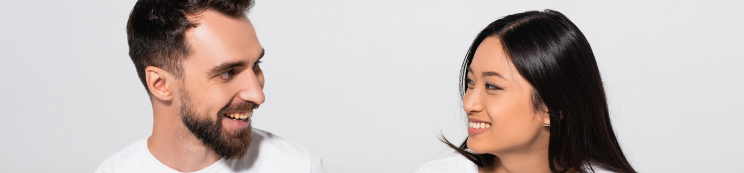 young interracial couple in white t-shirts looking at each other while sitting on white